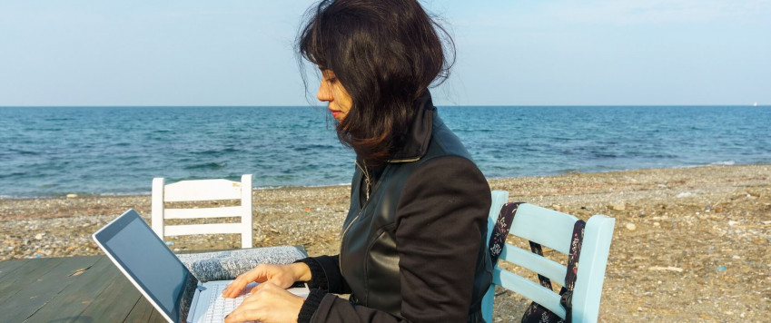 Ilustratīvs attēls sieviete ar datoru pludmalē